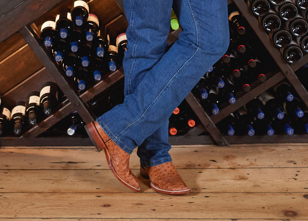 Un hombre que lleva botas occidentales Justin está de pie frente a un estante de vinos.